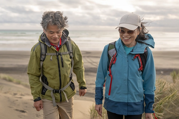 middle-aged couple in rain jackets walking on the beach